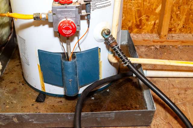 A water heater with connecting pipes and a pressure relief valve on a concrete floor.