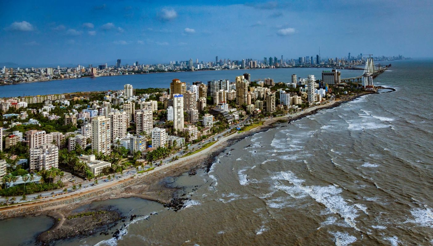 A panoramic view of a coastal city with high-rise buildings and waves lapping at the shore.