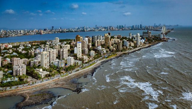 A panoramic view of a coastal city with high-rise buildings and waves lapping at the shore.