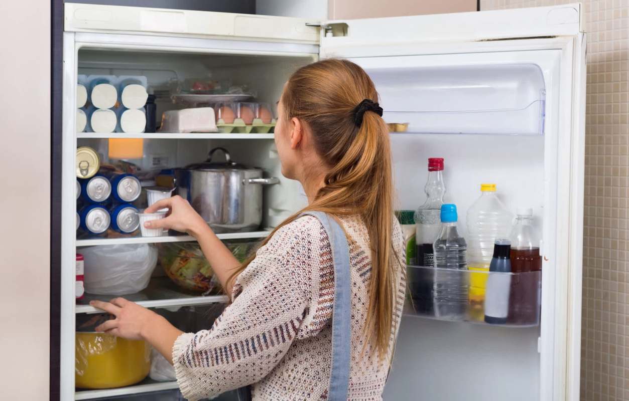 A person is reaching into a refrigerator filled with various food items and drinks.
