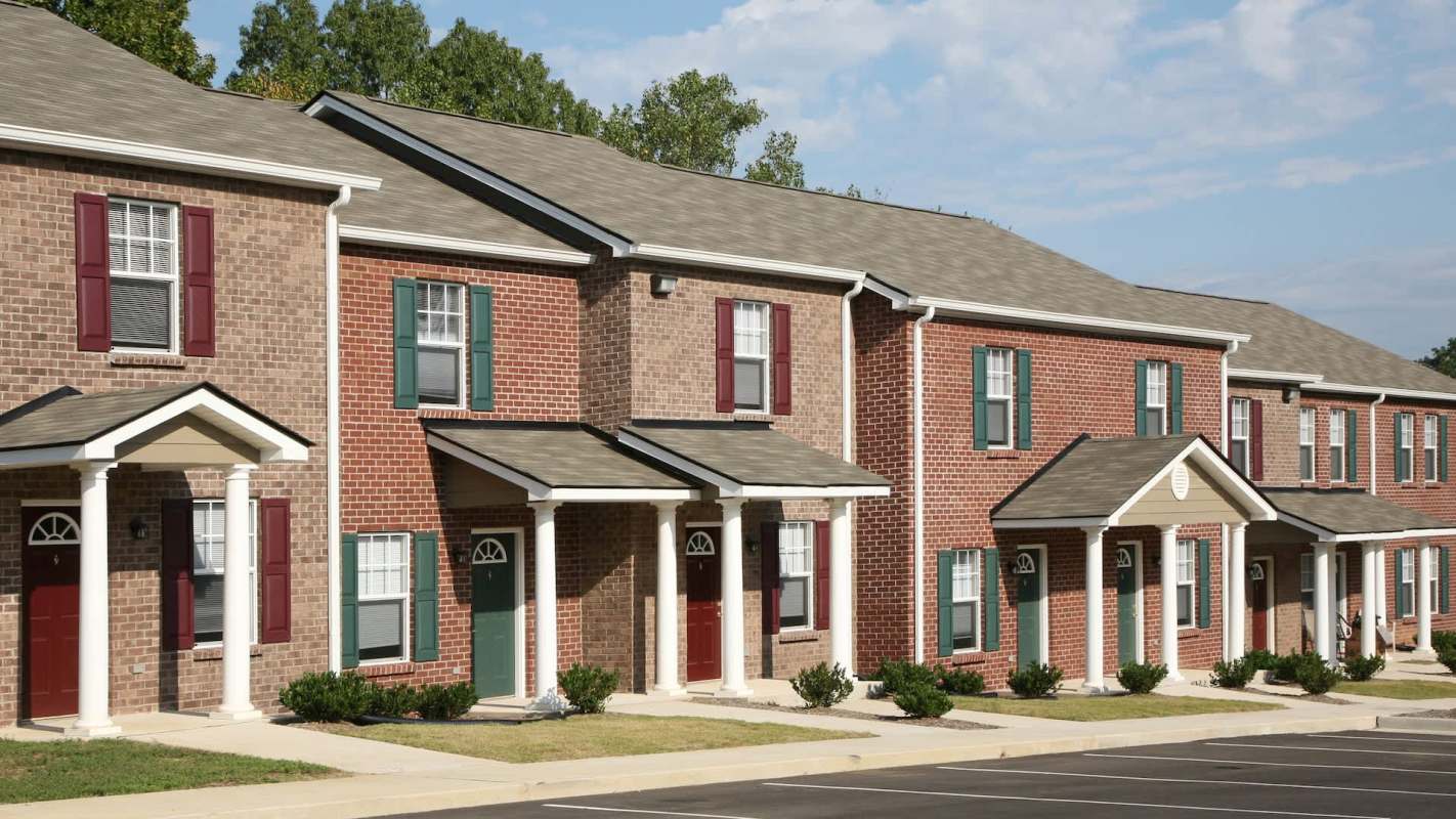 Rows of brick townhouses with various colored doors and landscaped front yards under a clear blue sky.