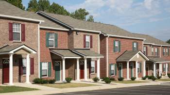 Rows of brick townhouses with various colored doors and landscaped front yards under a clear blue sky.