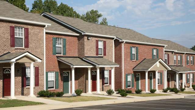 Rows of brick townhouses with various colored doors and landscaped front yards under a clear blue sky.