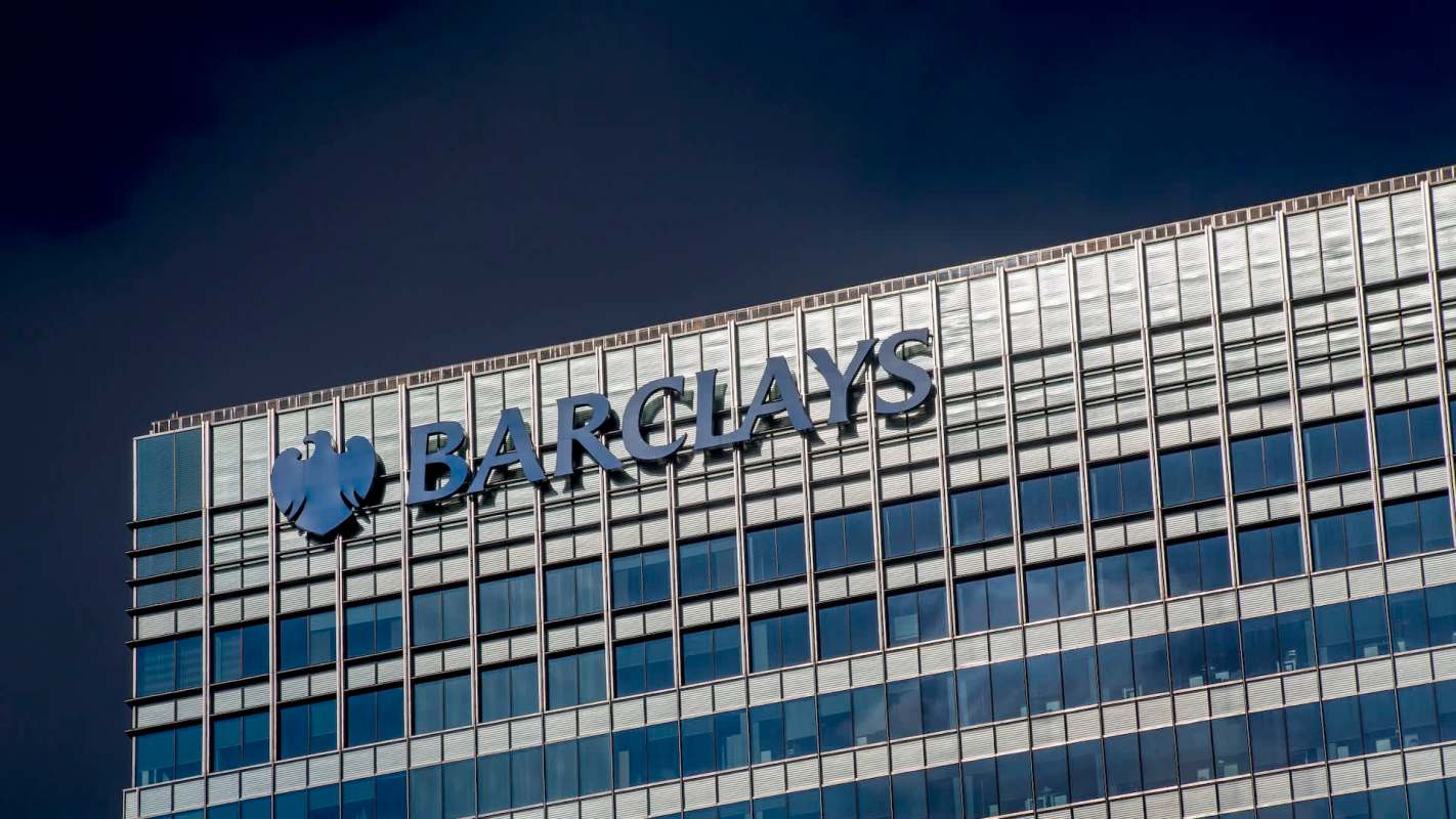 The Barclays logo on a modern glass building against a dark sky.