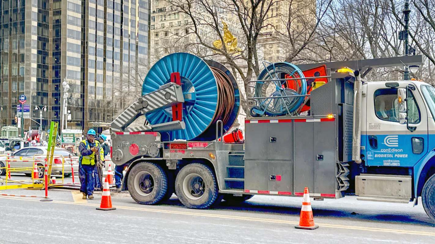 Workers in hard hats next to a construction truck with large spools of cable.
