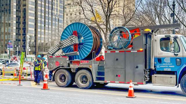 Workers in hard hats next to a construction truck with large spools of cable.