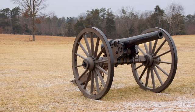 A historic cannon resting on a grassy field, surrounded by trees in the background.