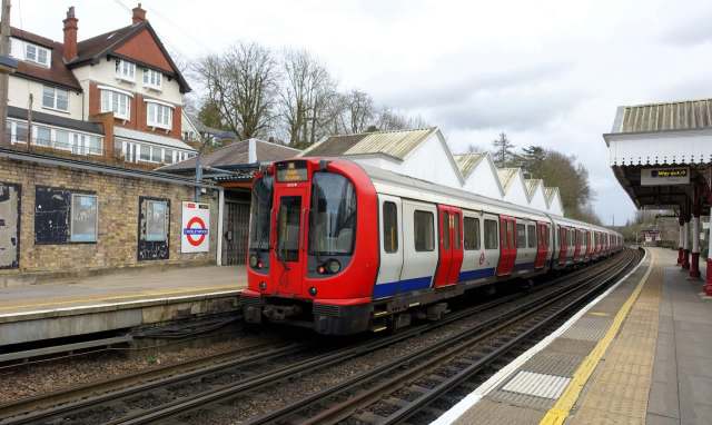 A train at a station with a "Chorleywood" sign and buildings in the background.