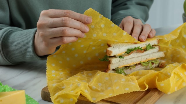 A hand wraps a sandwich with a beeswax wrap.