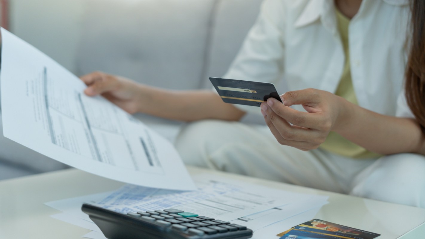 A person holding a credit card and reviewing documents.