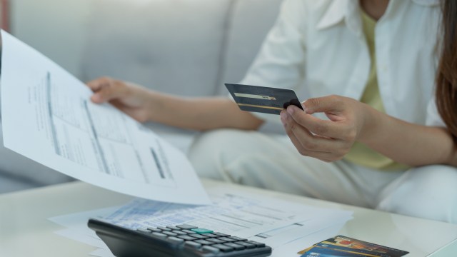 A person holding a credit card and reviewing documents.