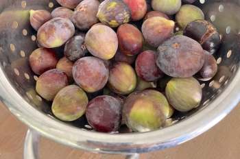 A close-up of a colander filled with ripe figs in various shades of purple and green.