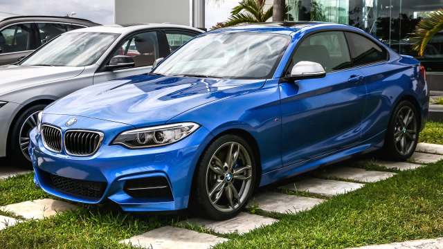 A blue BMW coupe parked on a grassy area next to other cars.