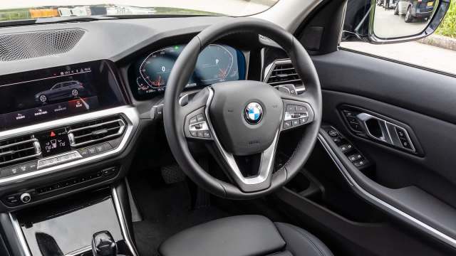 The interior of a BMW, featuring a steering wheel, digital dashboard, and center console controls.
