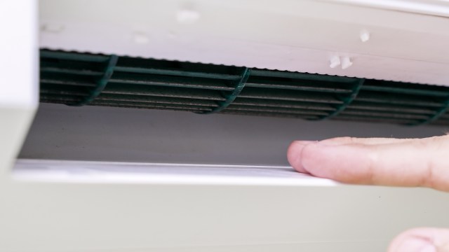 A hand reaching toward an HVAC vent.