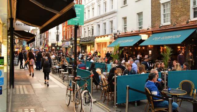 A busy street lined with restaurants and cafes filled with people dining outdoors.