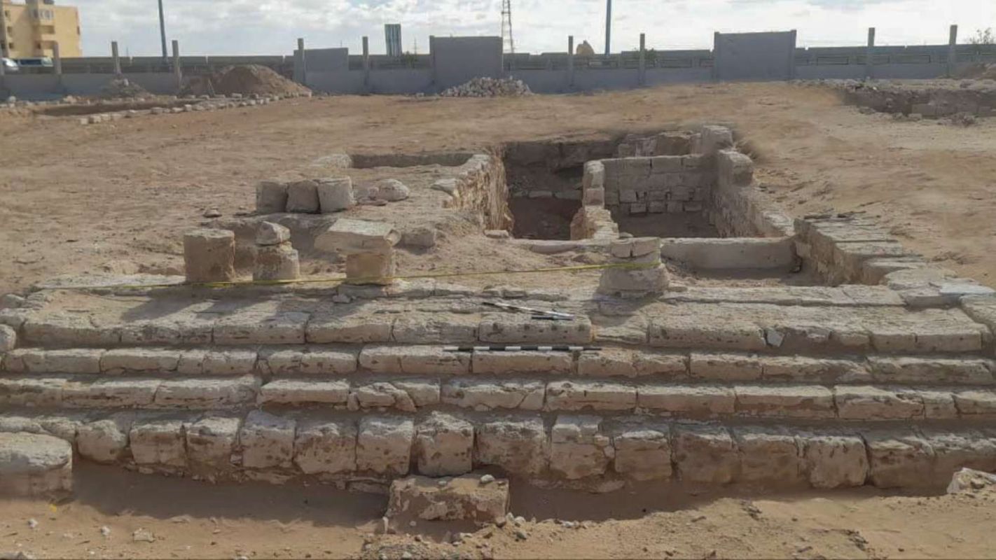 An archaeological site featuring exposed stone ruins and remnants of structures in a sandy landscape.