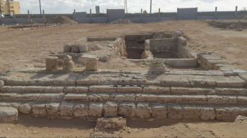 An archaeological site featuring exposed stone ruins and remnants of structures in a sandy landscape.