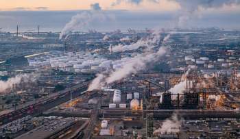An industrial area with storage tanks, factories, and smoke rising into the sky.