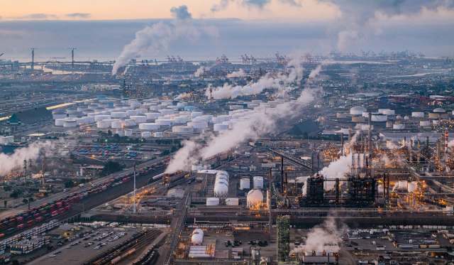 An industrial area with storage tanks, factories, and smoke rising into the sky.