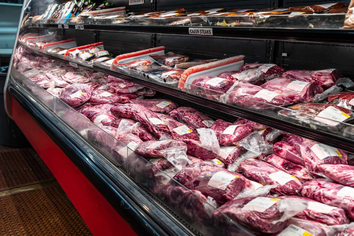 A refrigerated display case filled with various vacuum-sealed packages of beef cuts in a grocery store.