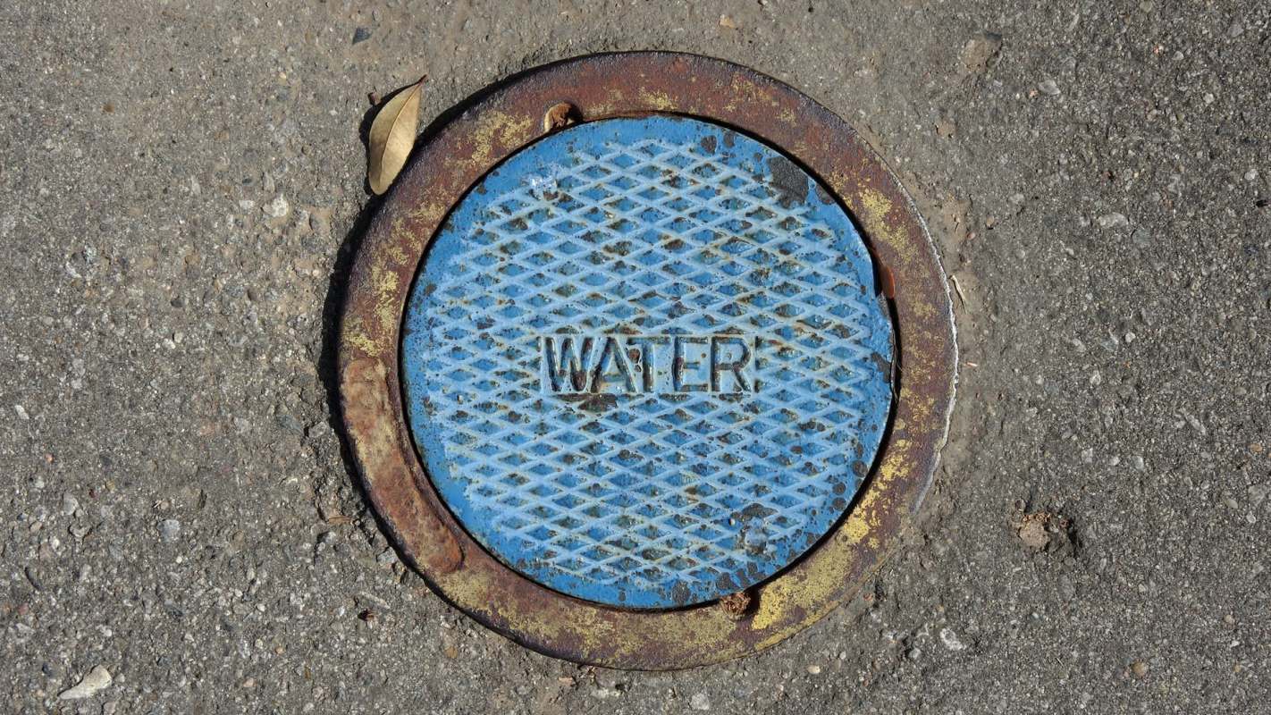 A blue manhole cover labeled "WATER" on a concrete surface.