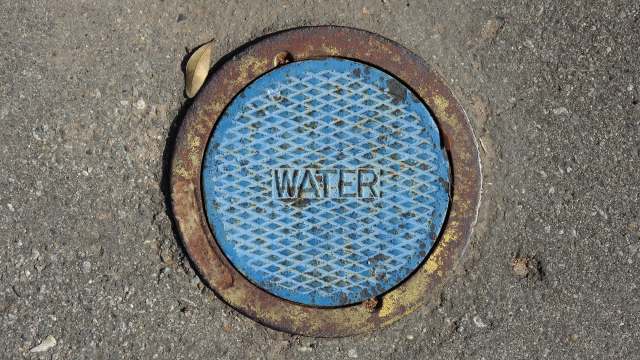 A blue manhole cover labeled "WATER" on a concrete surface.