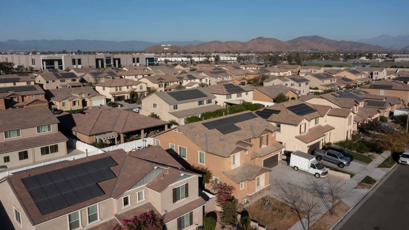 A residential neighborhood with houses featuring solar panels and mountains in the background.