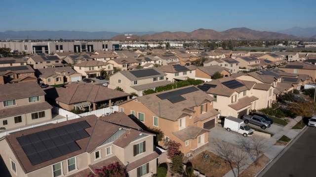 A residential neighborhood with houses featuring solar panels and mountains in the background.