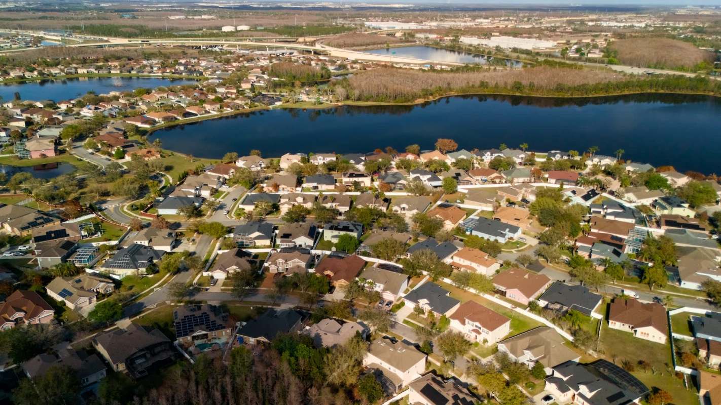 Aerial view of a suburban neighborhood with houses, lakes, and winding roads under a clear sky.