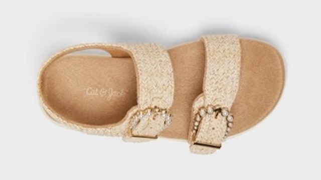 A close-up view of a stylish beige sandal with decorative buckles and a textured strap.