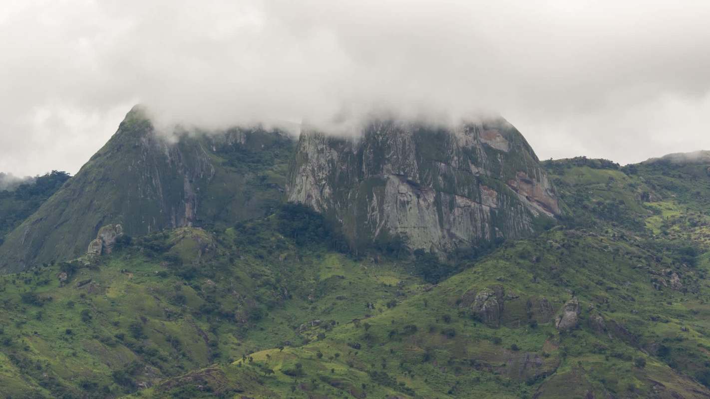 A mountainous landscape featuring green hills partially covered by clouds.