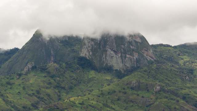 A mountainous landscape featuring green hills partially covered by clouds.