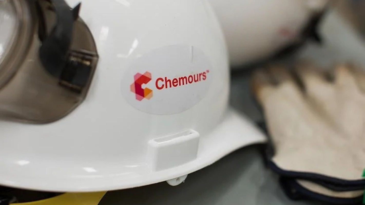 A close-up of a white safety helmet with a "Chemours" logo and a pair of gloves in the background.