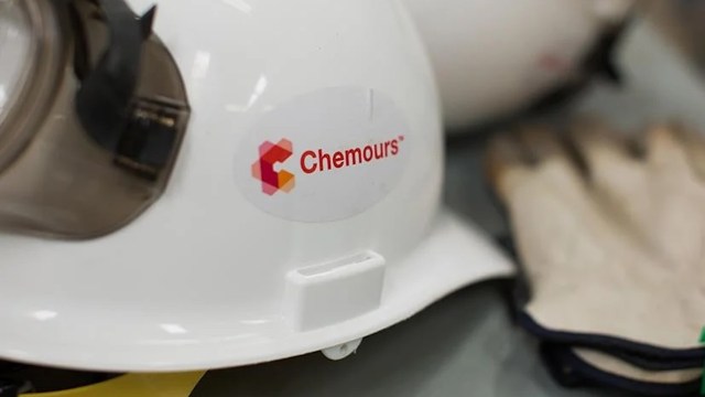 A close-up of a white safety helmet with a "Chemours" logo and a pair of gloves in the background.