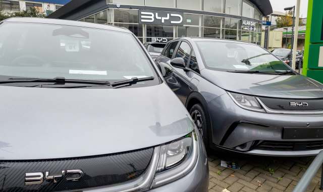 Two silver BYD electric cars are parked close together in front of a dealership.