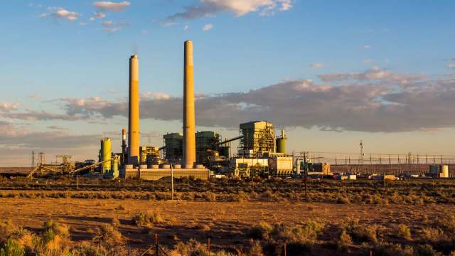 A power plant with two tall smokestacks and industrial structures under a blue sky with scattered clouds.