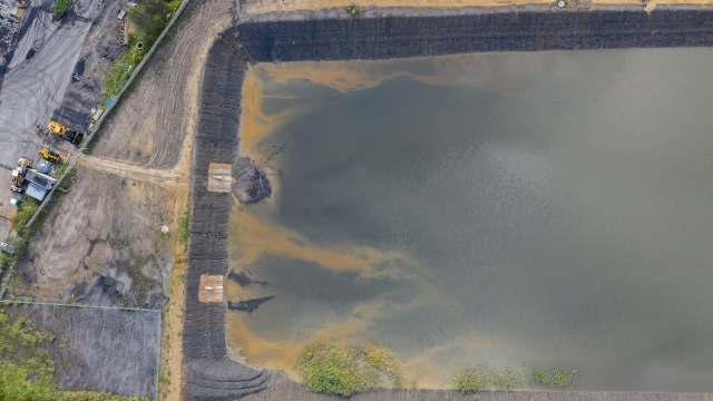An aerial view of a large, muddy water body bordered by coal ash and machinery in an industrial area.