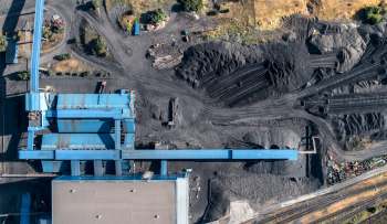 An aerial view of a coal storage facility with blue structures and piles of coal on a gray terrain.