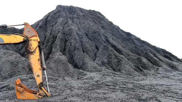 A mound of black coal with an excavator bucket positioned in the foreground.