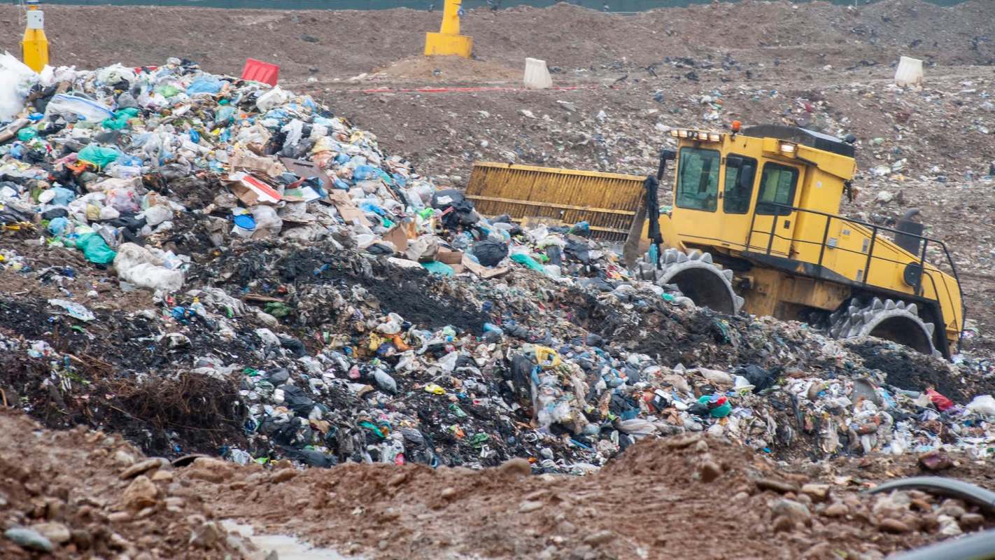 A bulldozer moving piles of garbage at a landfill.