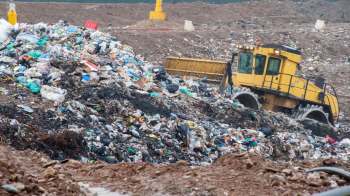 A bulldozer moving piles of garbage at a landfill.