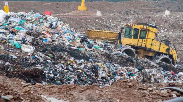 A bulldozer moving piles of garbage at a landfill.