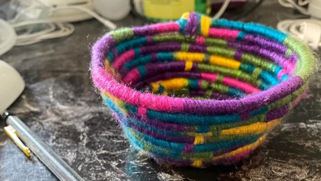 A colorful woven basket featuring vibrant purple, pink, blue, and green yarn patterns.