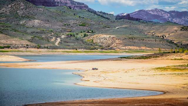 A serene lake bordered by sandy shores and rolling green hills under a partly cloudy sky.