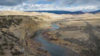 A winding river flows through a dry, hilly landscape under a cloudy sky.
