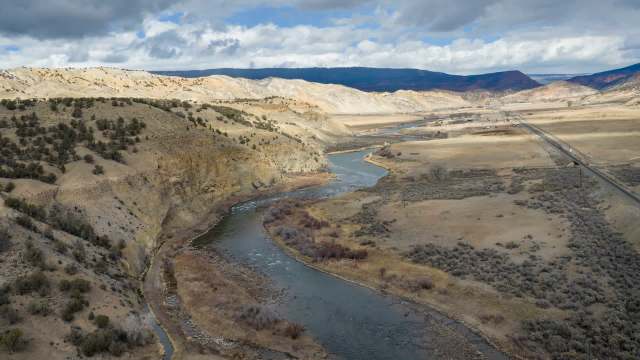 A winding river flows through a dry, hilly landscape under a cloudy sky.