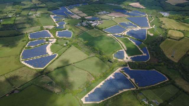Aerial view of vast solar farms interspersed among green fields and farmland in a rural landscape.