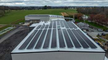A rooftop covered in solar panels with agricultural fields and buildings in the background.