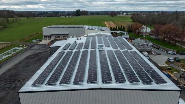 A rooftop covered in solar panels with agricultural fields and buildings in the background.